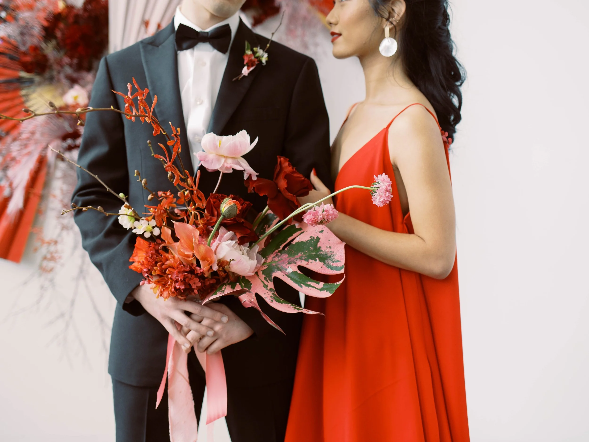 Close-up of the couple with a vibrant bouquet of red, pink and painted tropical foliage