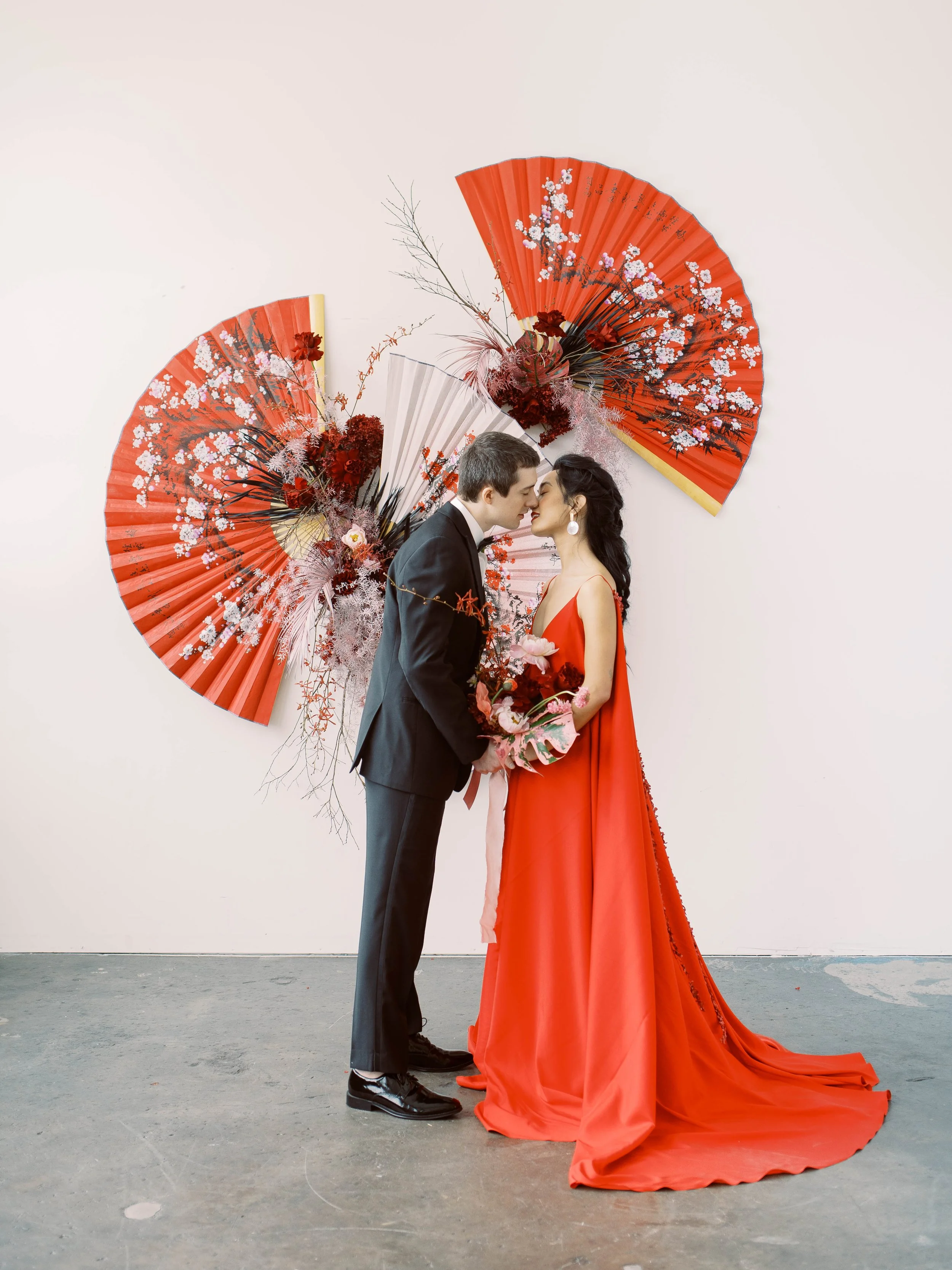 Couple in formal attire standing beneath red decorative fans and florals during a Lunar New Year elopement.