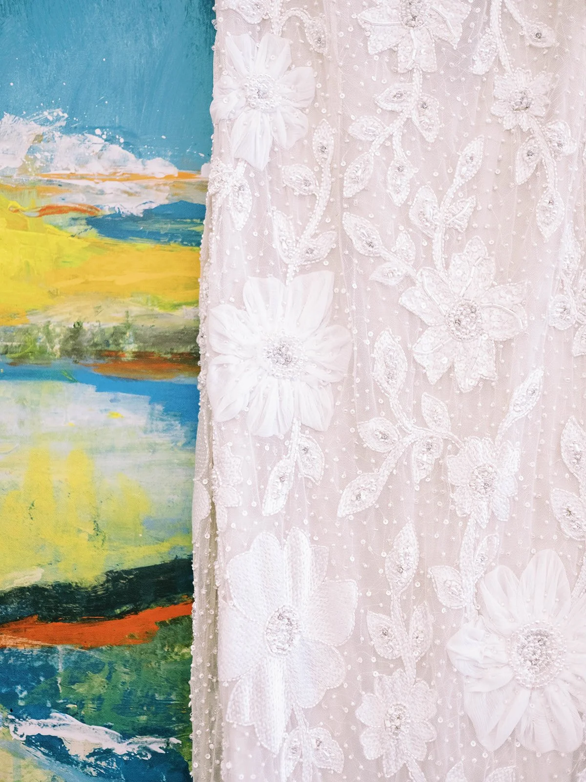 Beaded white wedding dress displayed beside a colorful abstract painting at Leach Botanical Garden.