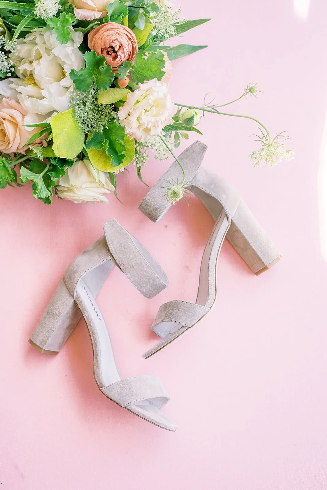 Beige block-heel wedding shoes beside a colorful bouquet of roses, ranunculus and greenery.