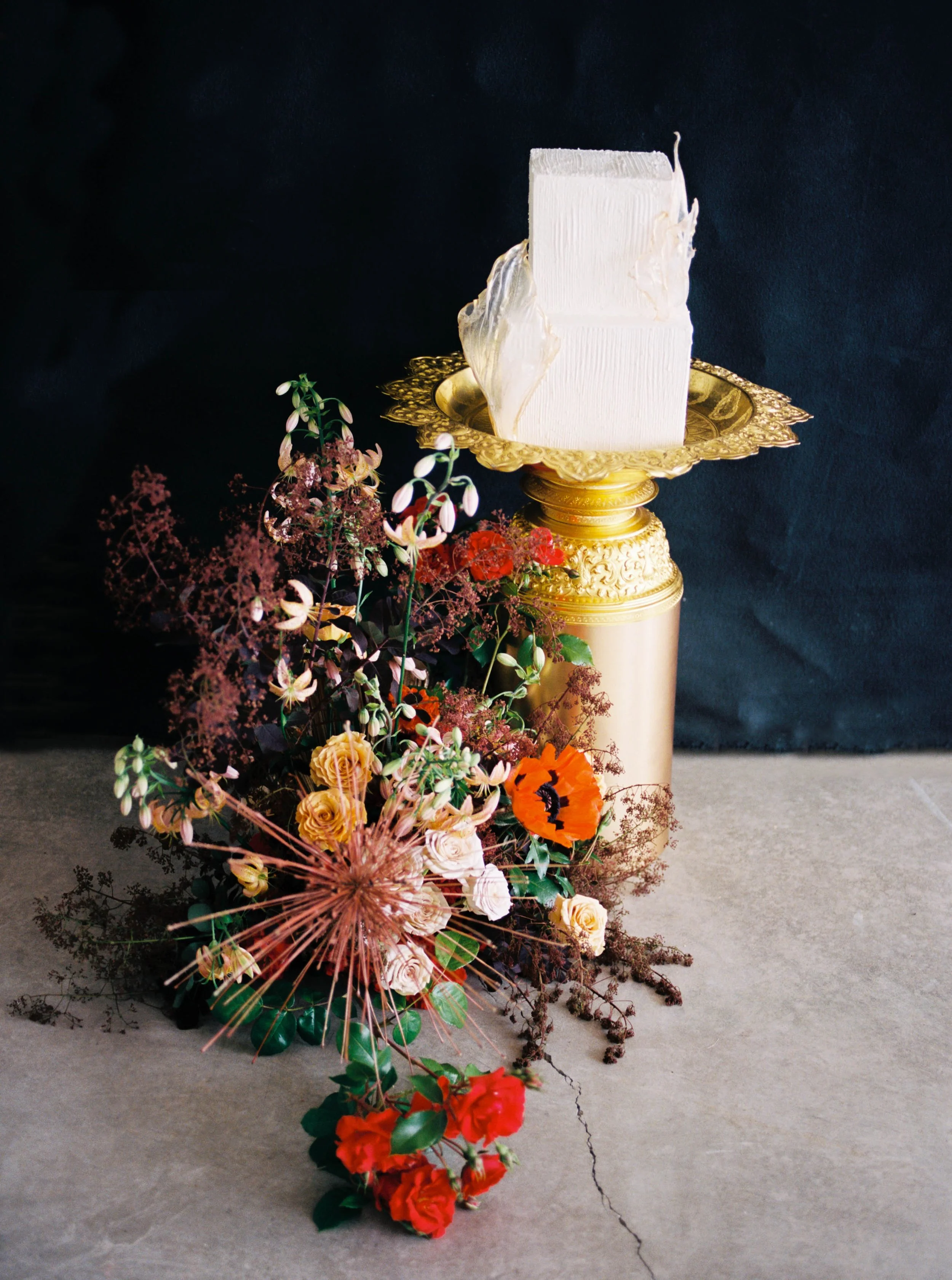 Modern white wedding cake displayed beside an asymmetrical arrangement of colorful flowers.