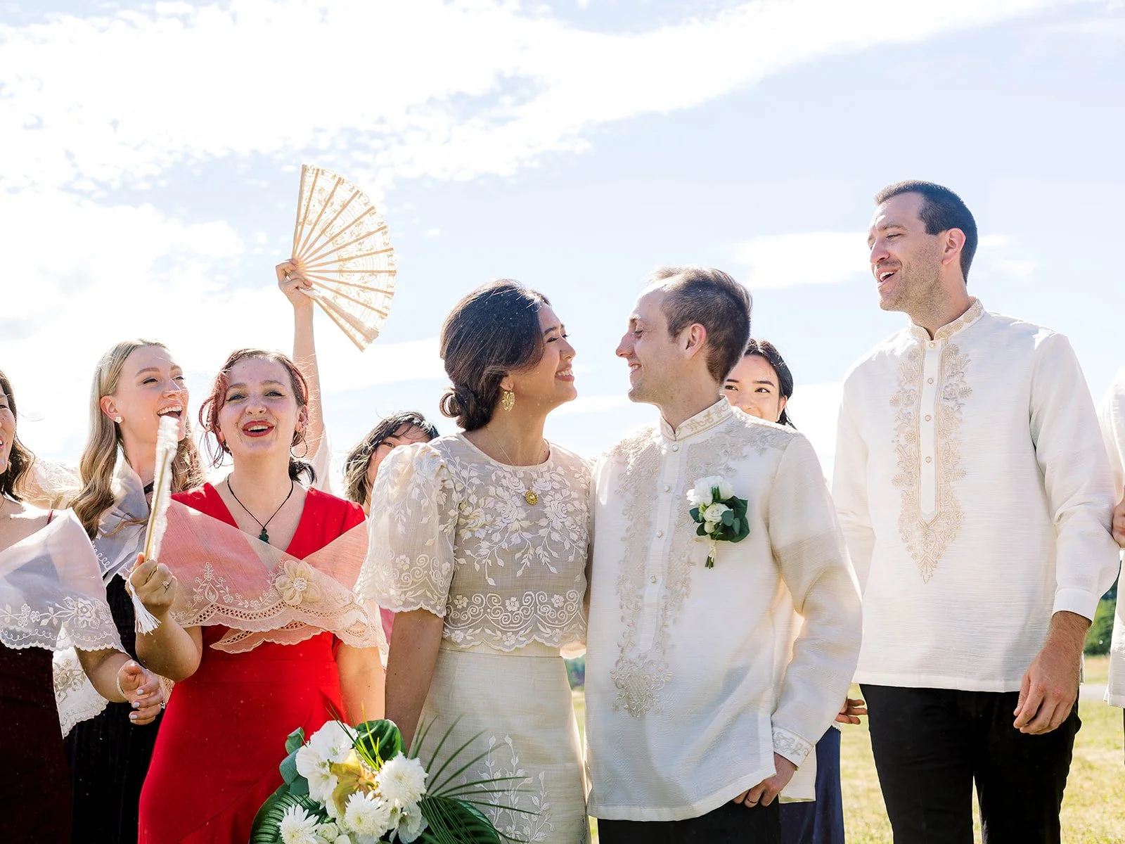 Wedding couple in embroidered Filipino attire surrounded by their wedding party outdoors.