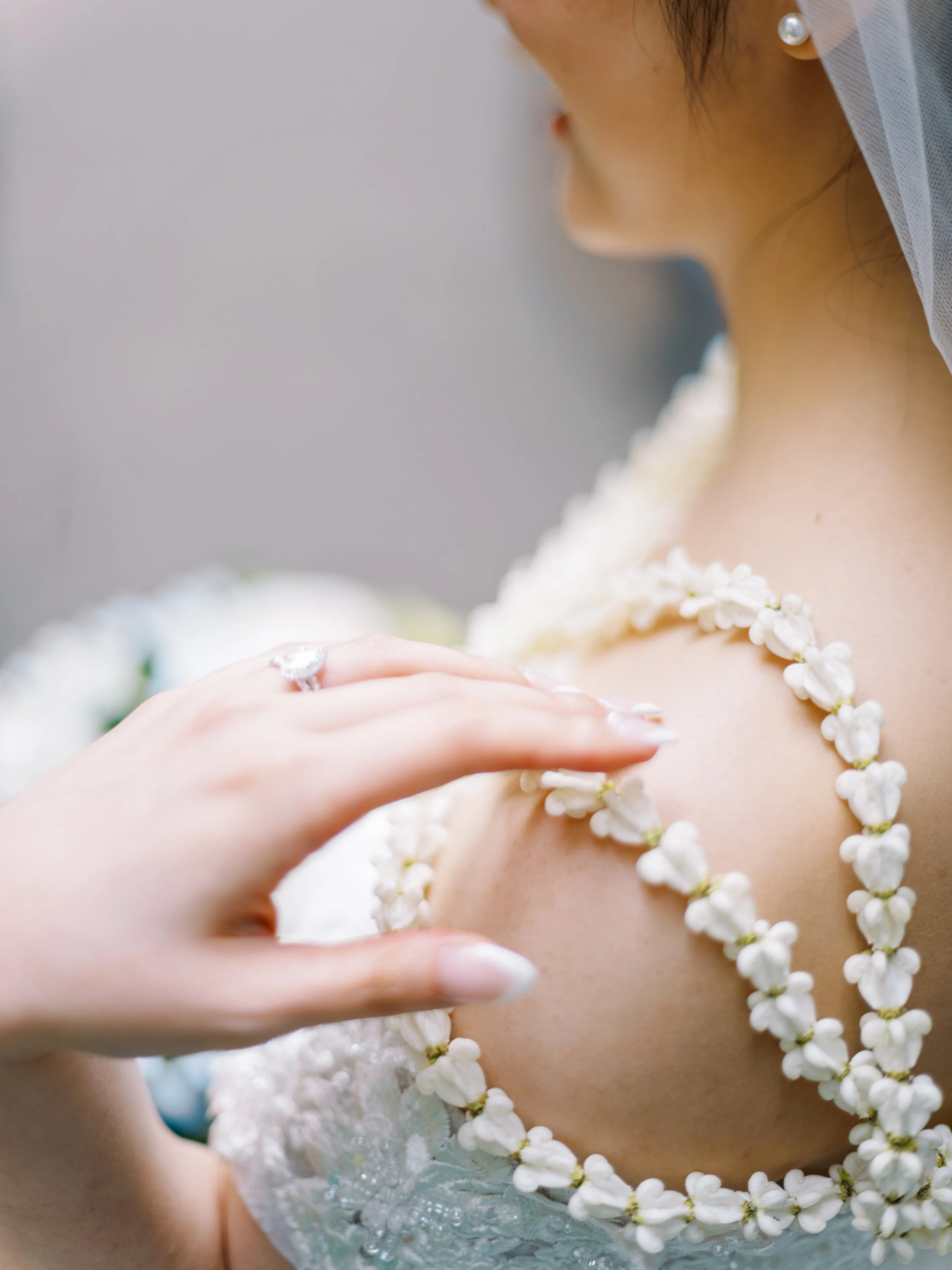 Close-up of the bride touching the white pua kalaunu flowers draped over her shoulder.