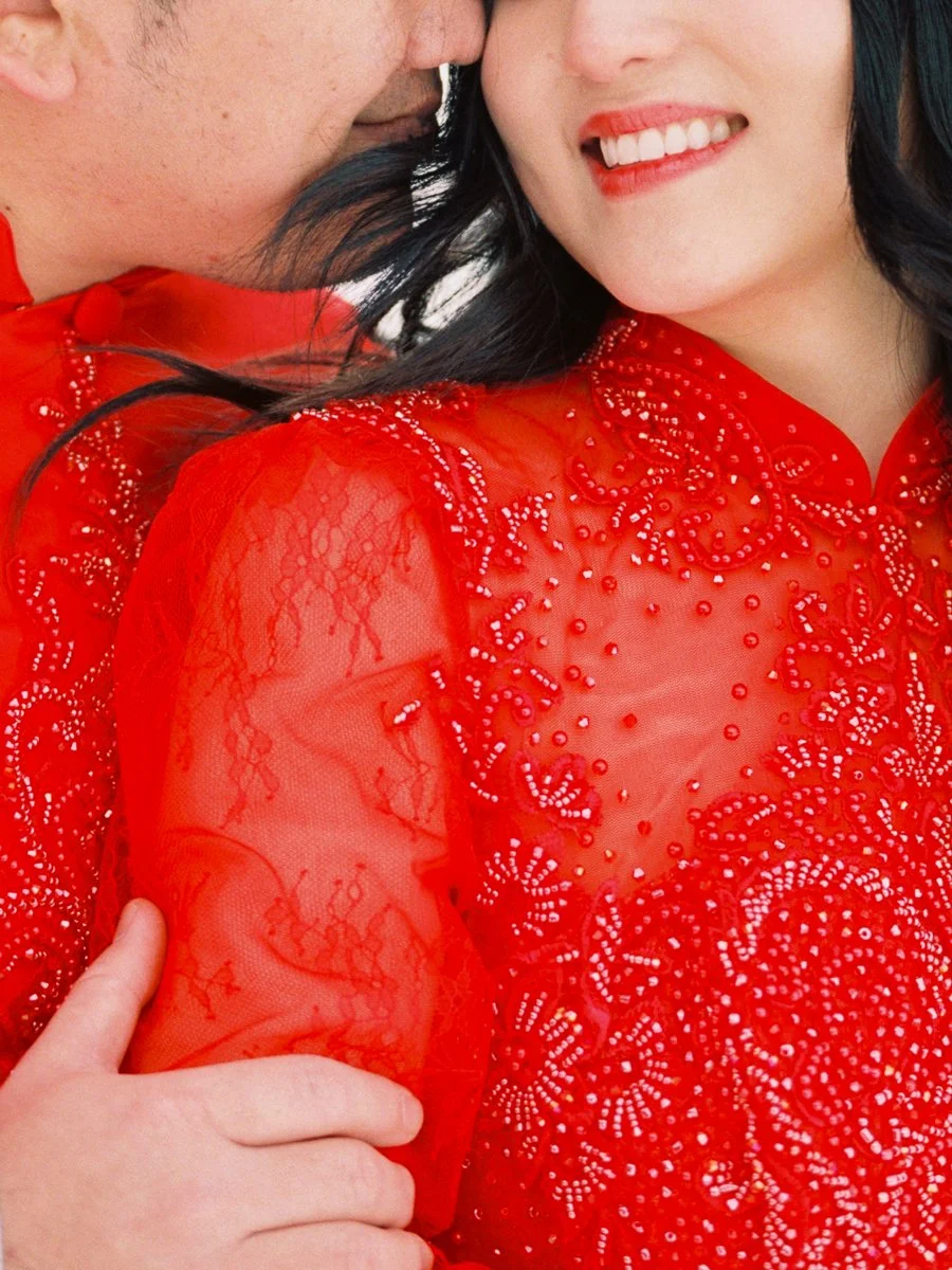 Close-up of a couple in red áo dài, highlighting the detailed beadwork on the woman’s dress and their close embrace.