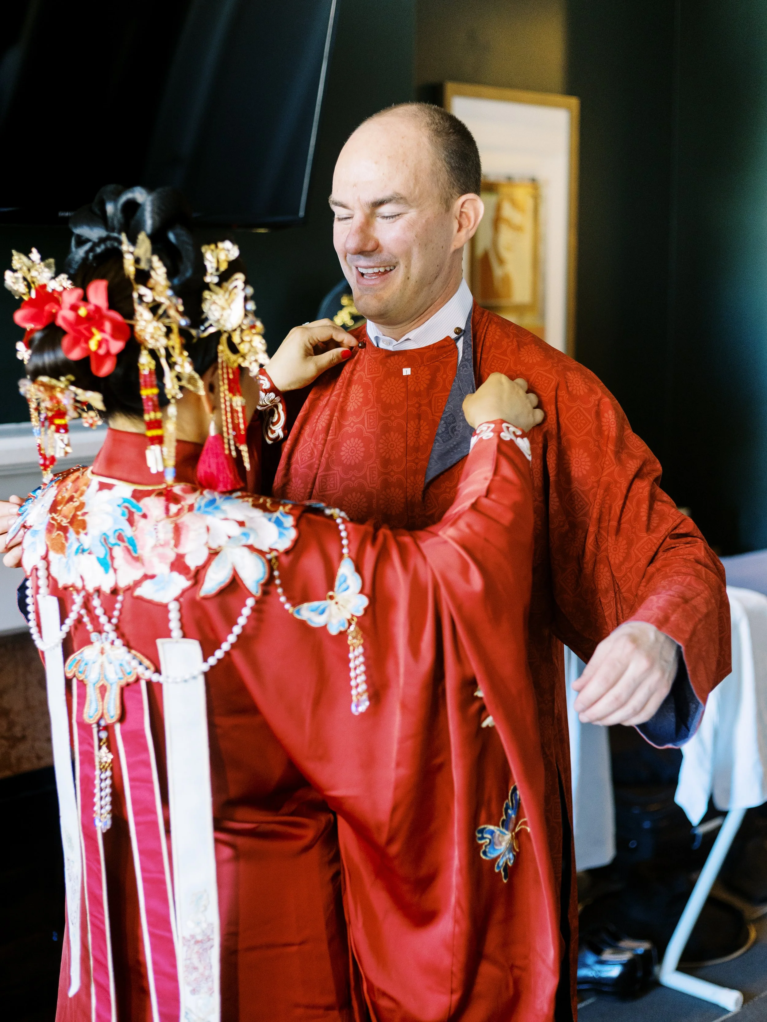 Bride helps the groom adjust his traditional Chinese wedding attire during wedding preparations before their Lan Su Chinese Garden ceremony in Portland.