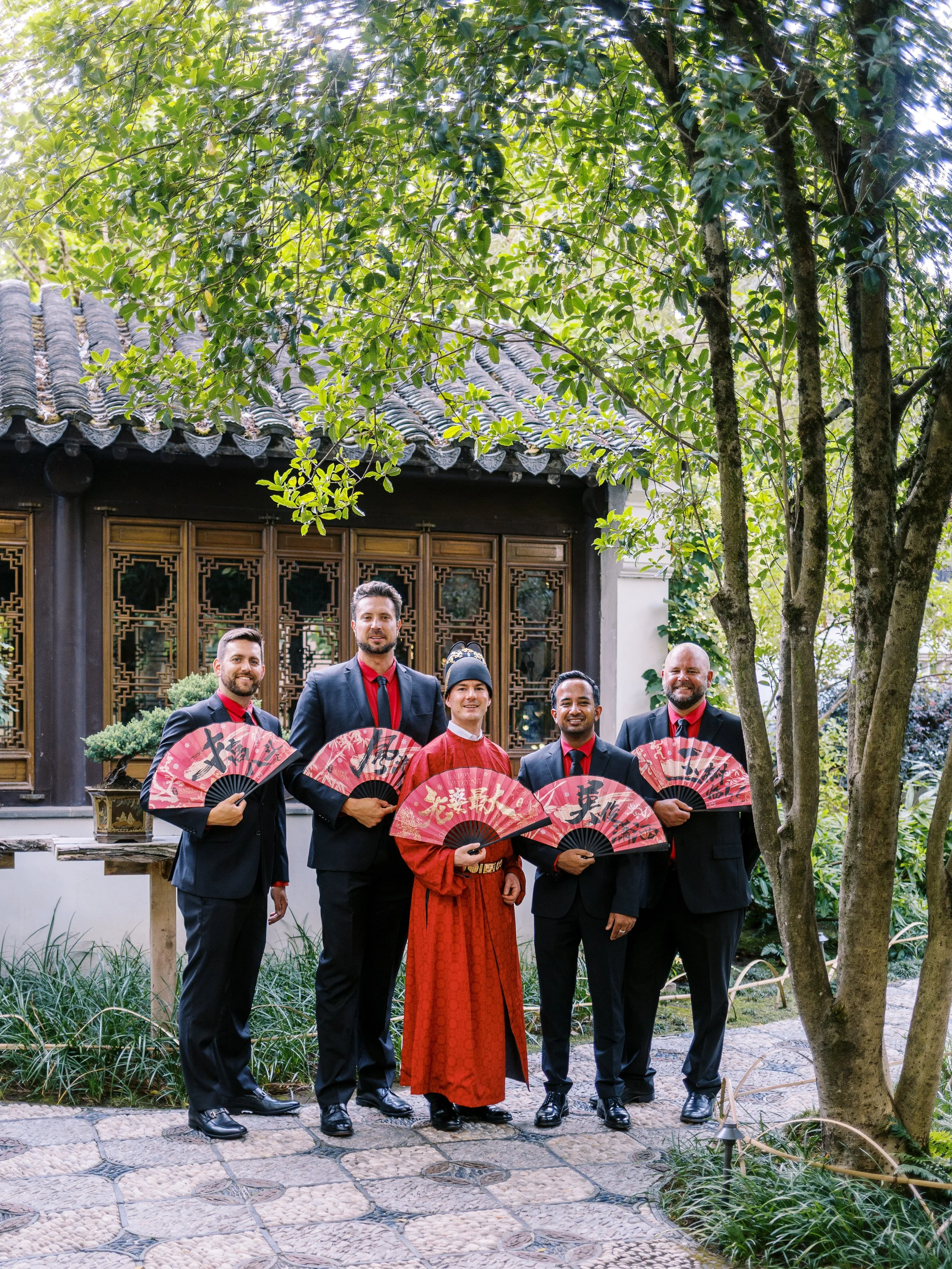 Groom and groomsmen posing with traditional fans at Lan Su Chinese Garden in Portland, dressed in coordinated wedding attire.