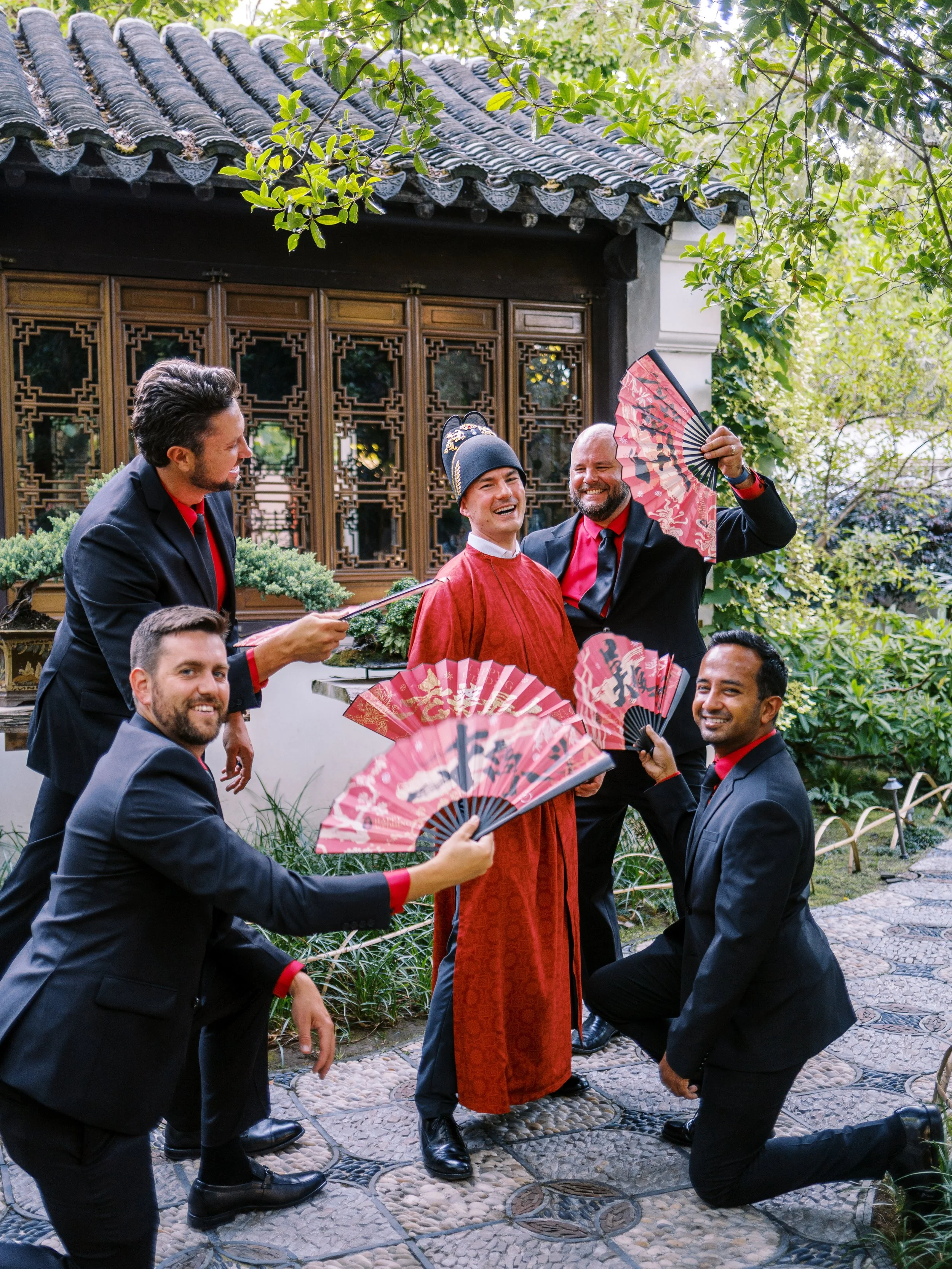 Groom laughing with groomsmen holding traditional fans during a joyful moment at a Lan Su Chinese Garden wedding in Portland.