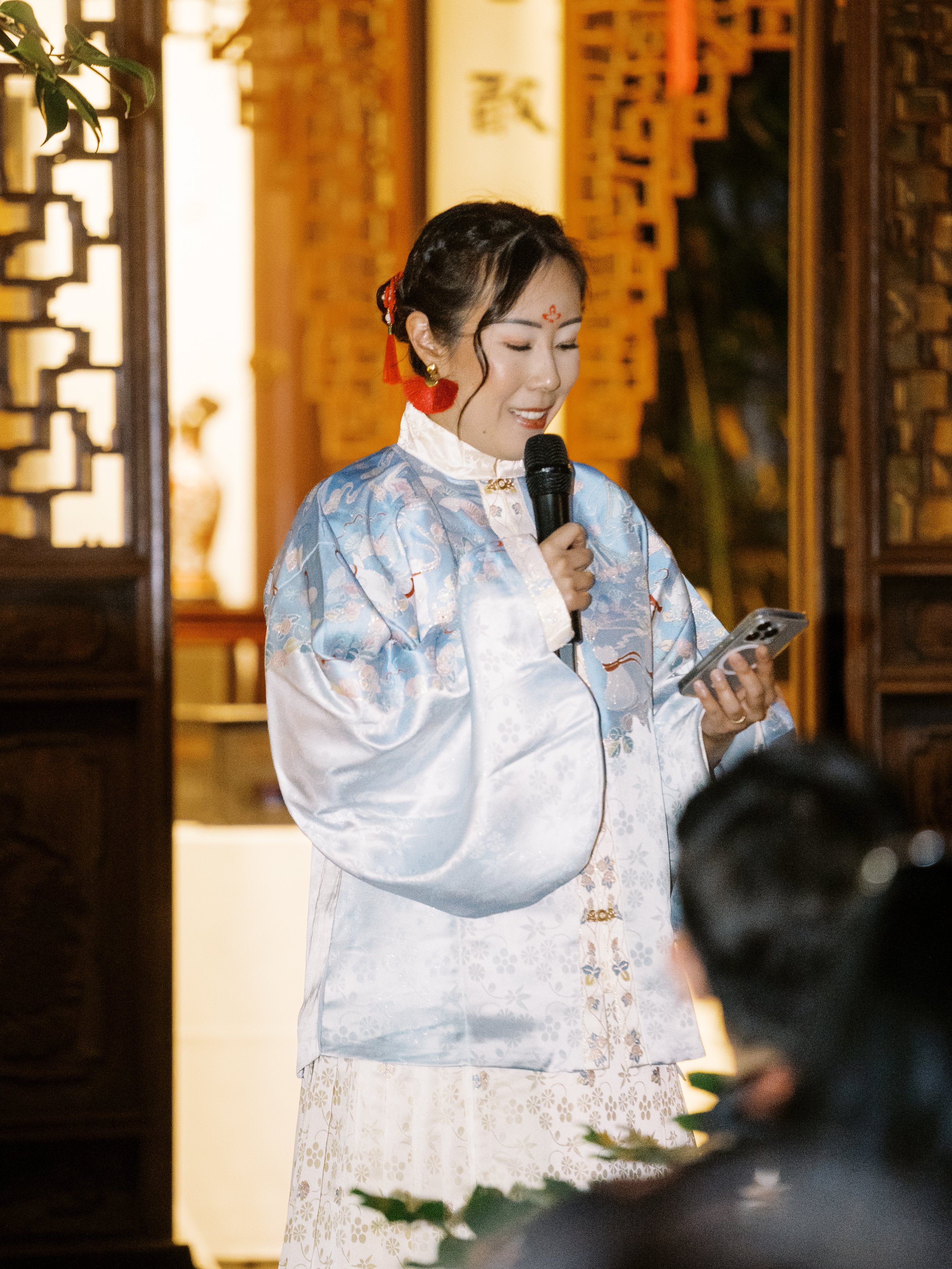 Bride wearing traditional attire giving a speech during her Lan Su Chinese Garden wedding reception.
