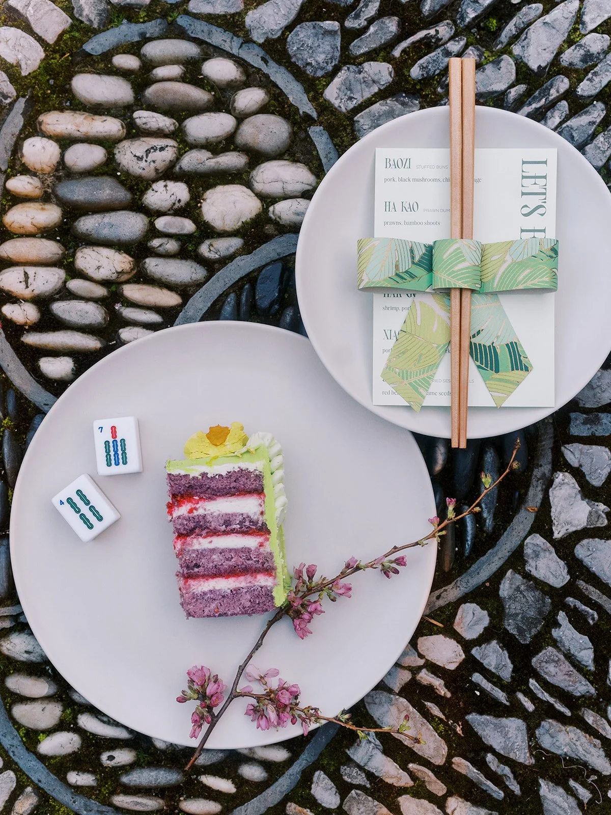 Styled place settings with dim sum menus, chopsticks, mahjong tiles, florals, and cake arranged for a couture bachelorette party at Lan Su Chinese Garden.
