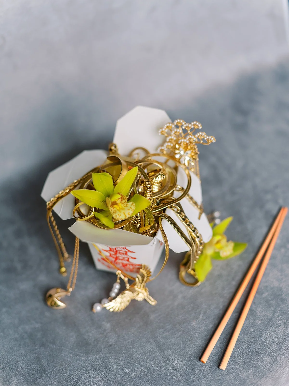 Gold jewelry, orchids, and mahjong tiles styled in a takeout box for a couture bachelorette party flat lay.