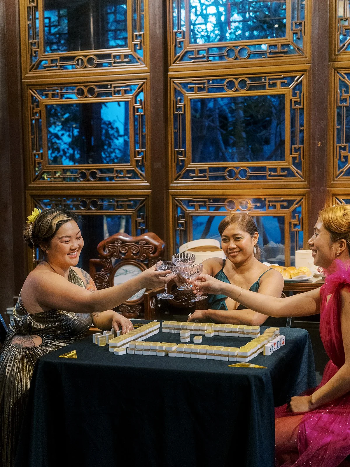 Friends clinking glasses over a mahjong table inside Lan Su Chinese Garden during a couture bachelorette party.