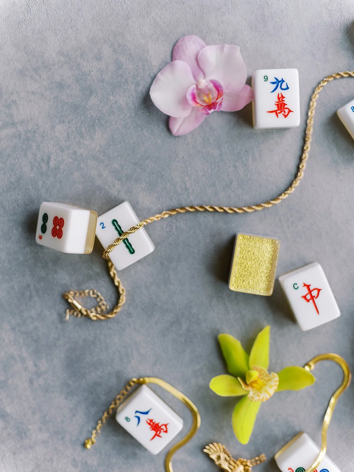 Flat lay of mahjong tiles, gold chain, and orchids styled for a glamorous bachelorette celebration.