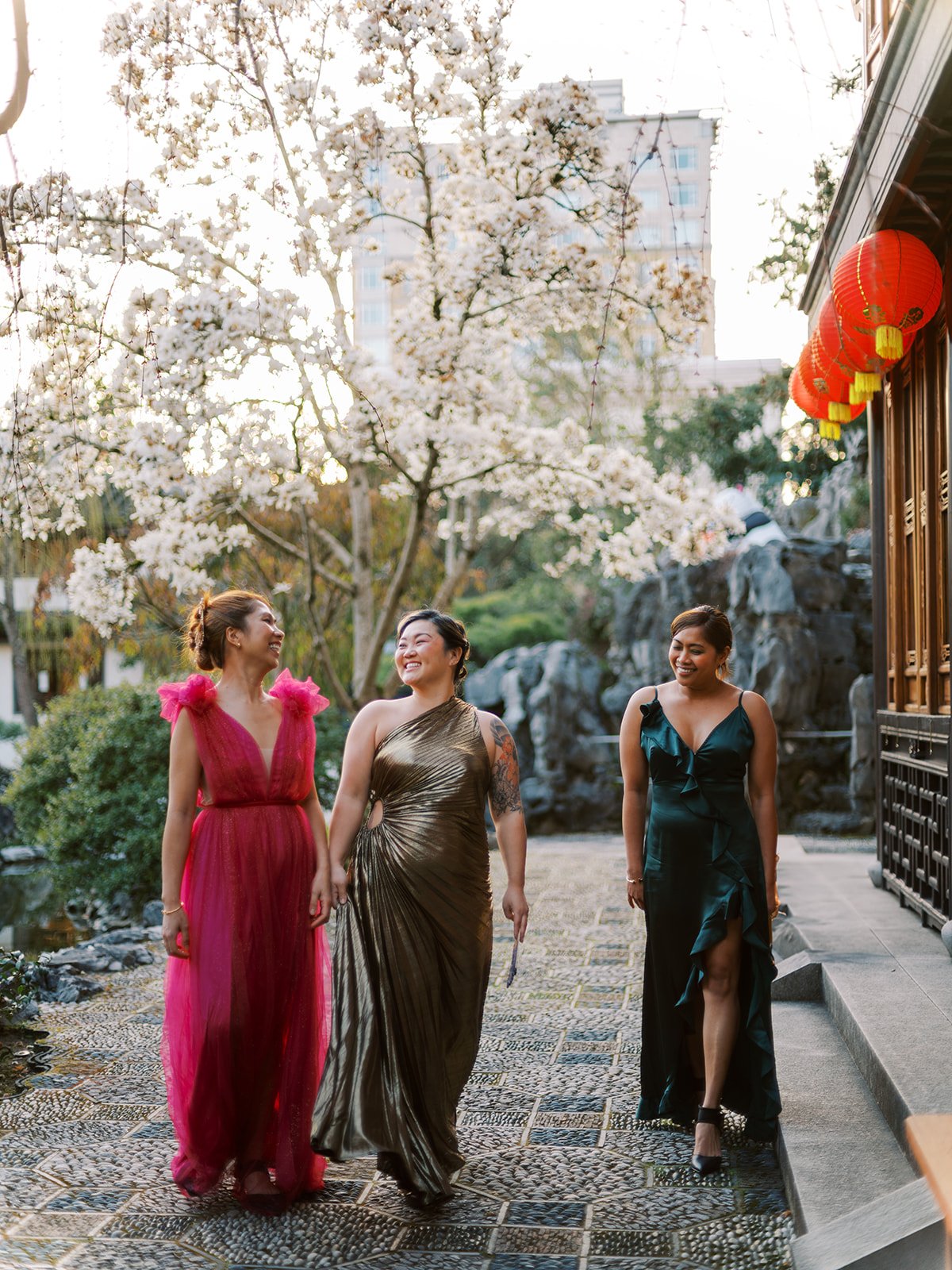 Three women in couture gowns walking through Lan Su Chinese Garden during a stylish bachelorette photoshoot.