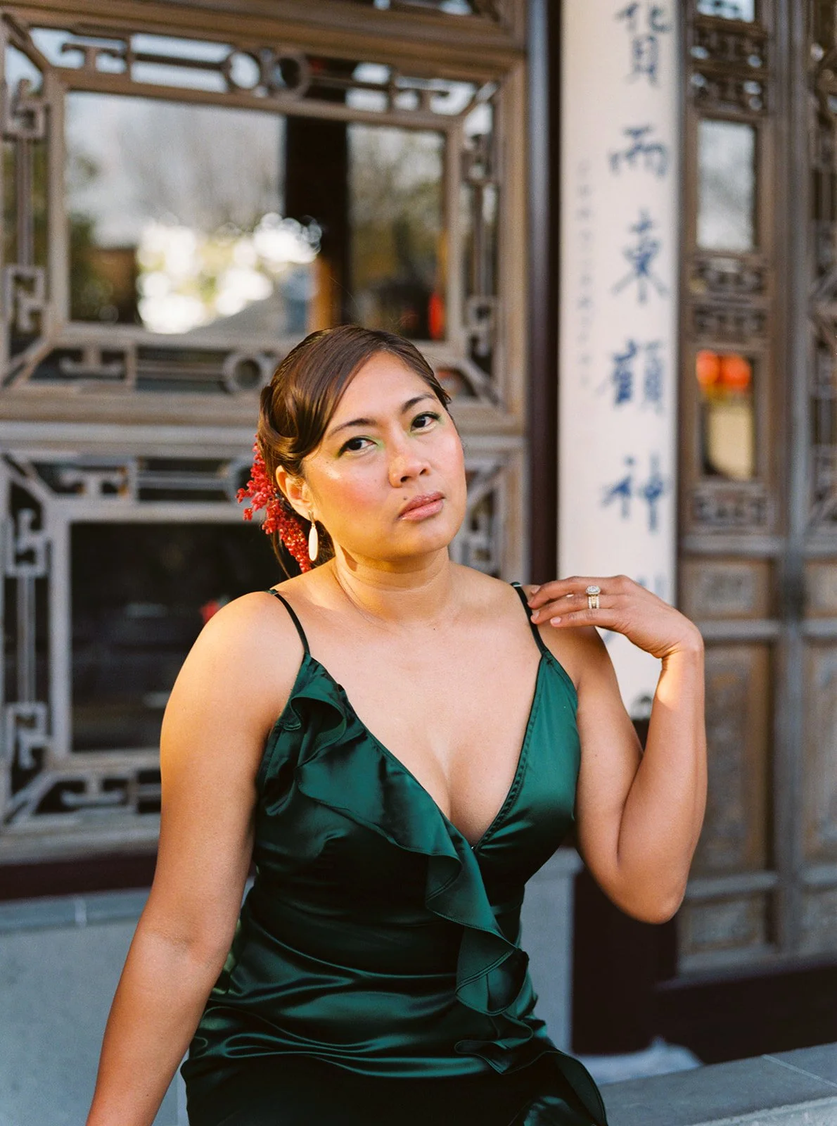 Woman in an emerald green gown posing against carved wood architecture at Lan Su Chinese Garden.