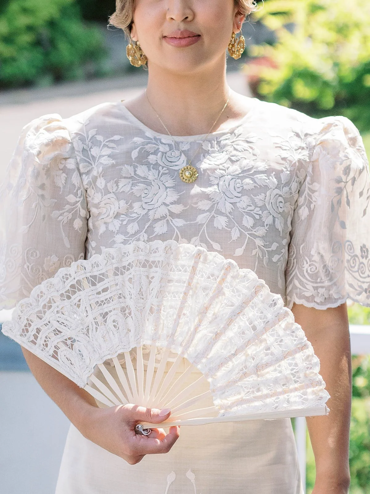Portrait detail of the bride holding a lace hand fan, highlighting the embroidered Filipiniana blouse and gold jewelry.