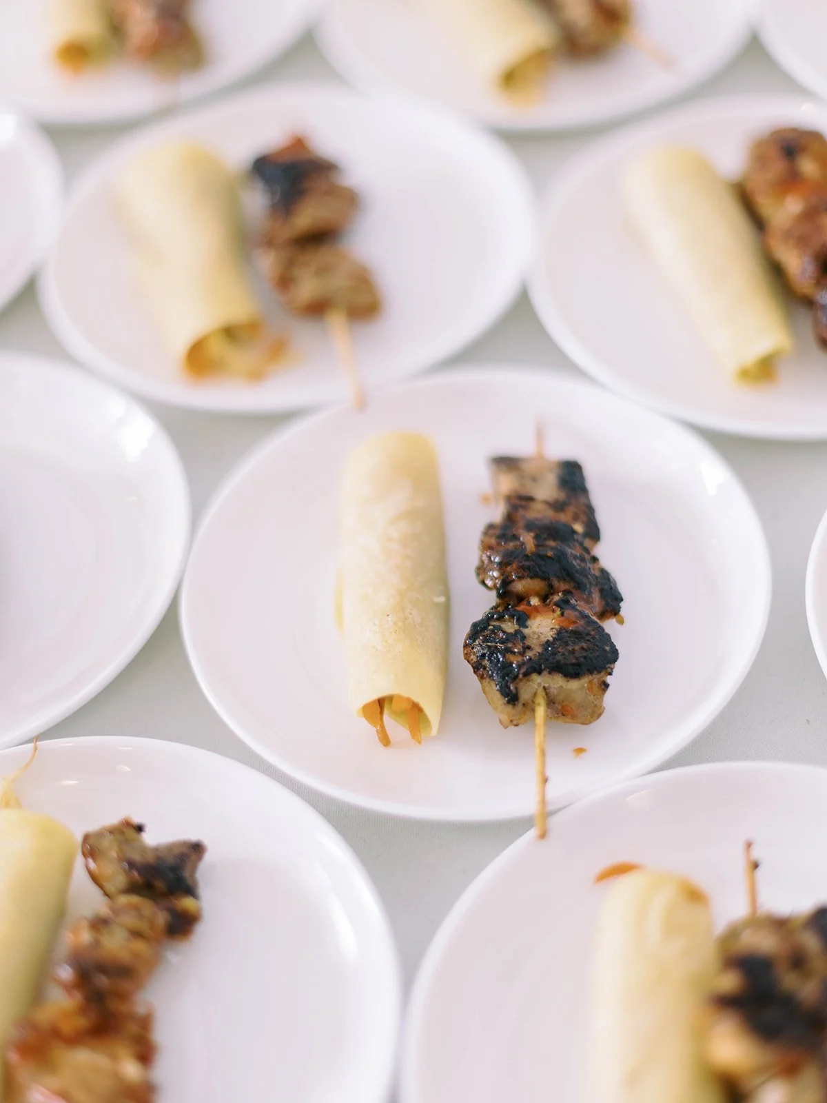 Plated Filipino wedding appetizers featuring lumpia and grilled skewers arranged on white plates for the reception.