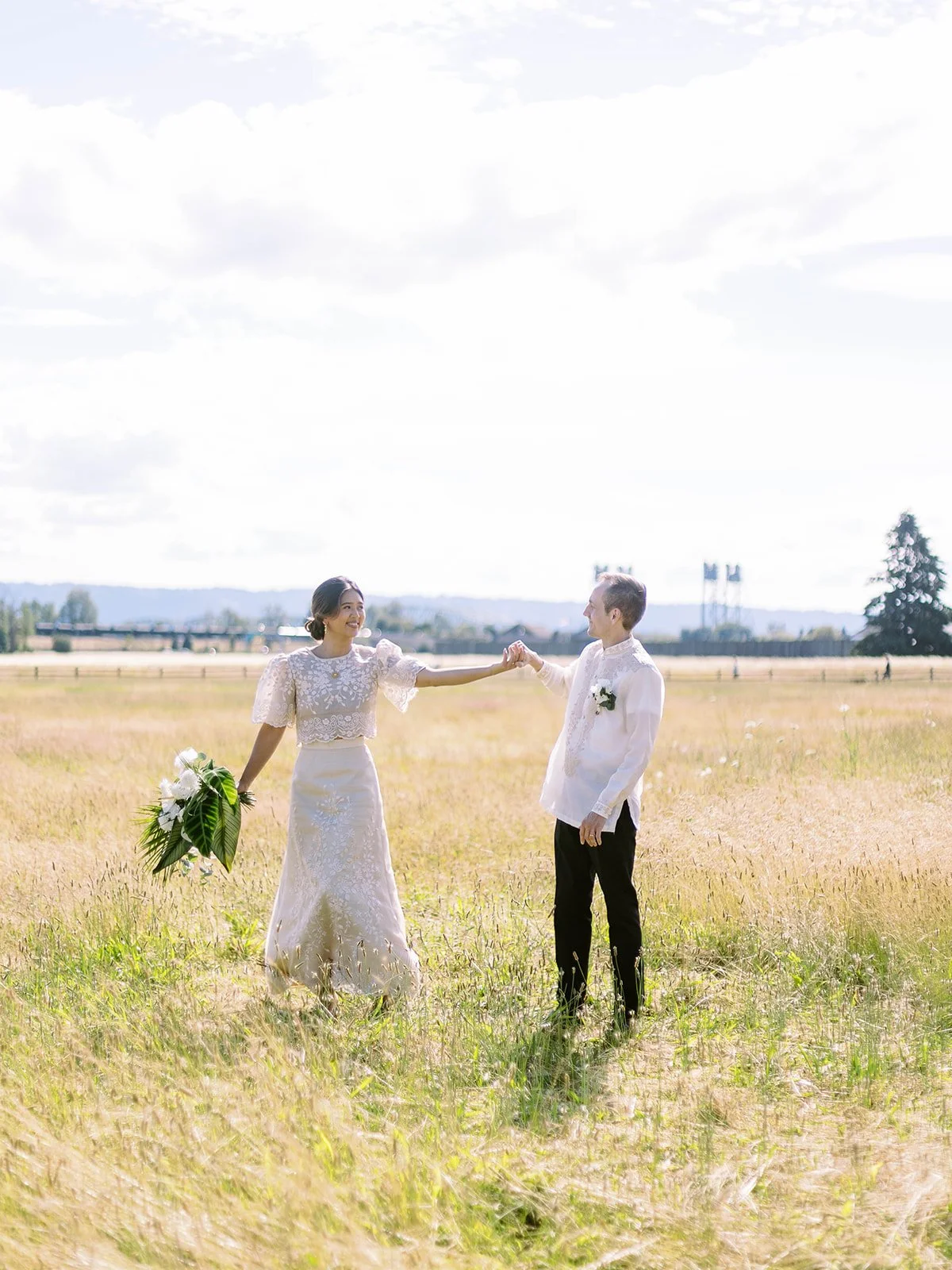Bride and groom holding hands while walking through an open field near Pearson Air Museum, dressed in Filipiniana and Barong Tagalog.