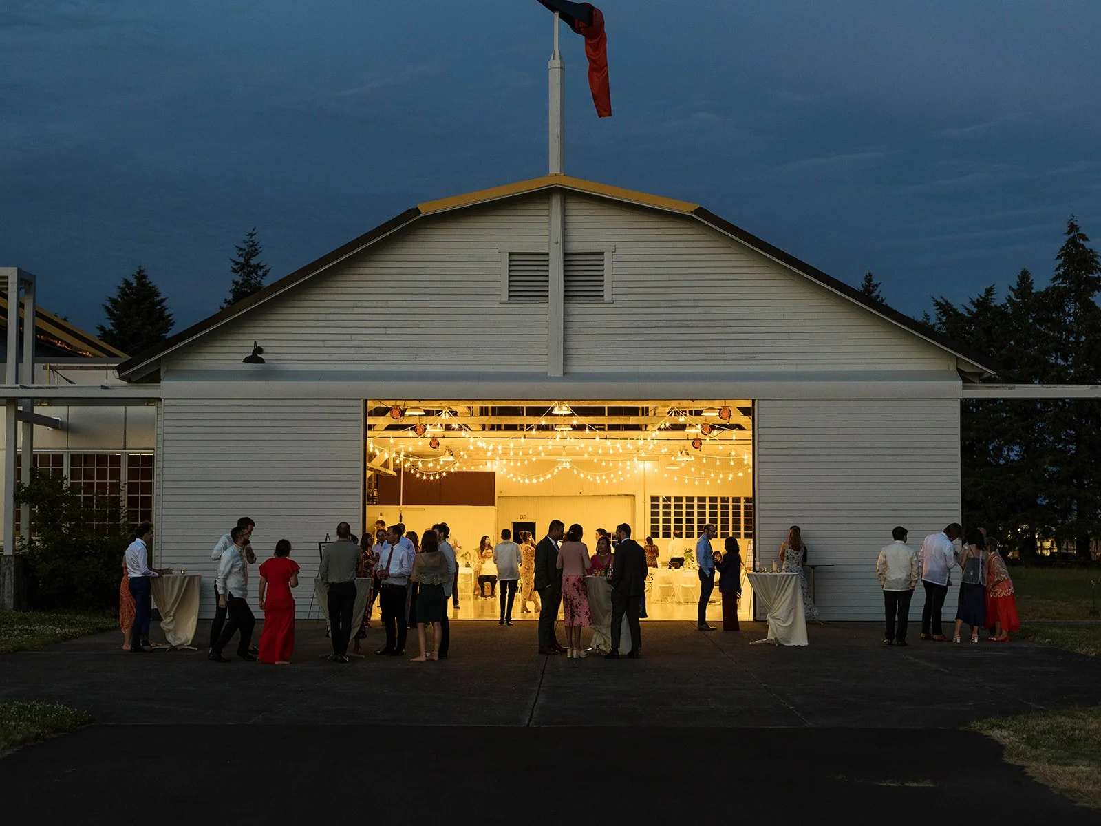 Twilight exterior of the Pearson Air Museum hangar glowing with string lights as guests gather outside the wedding reception.