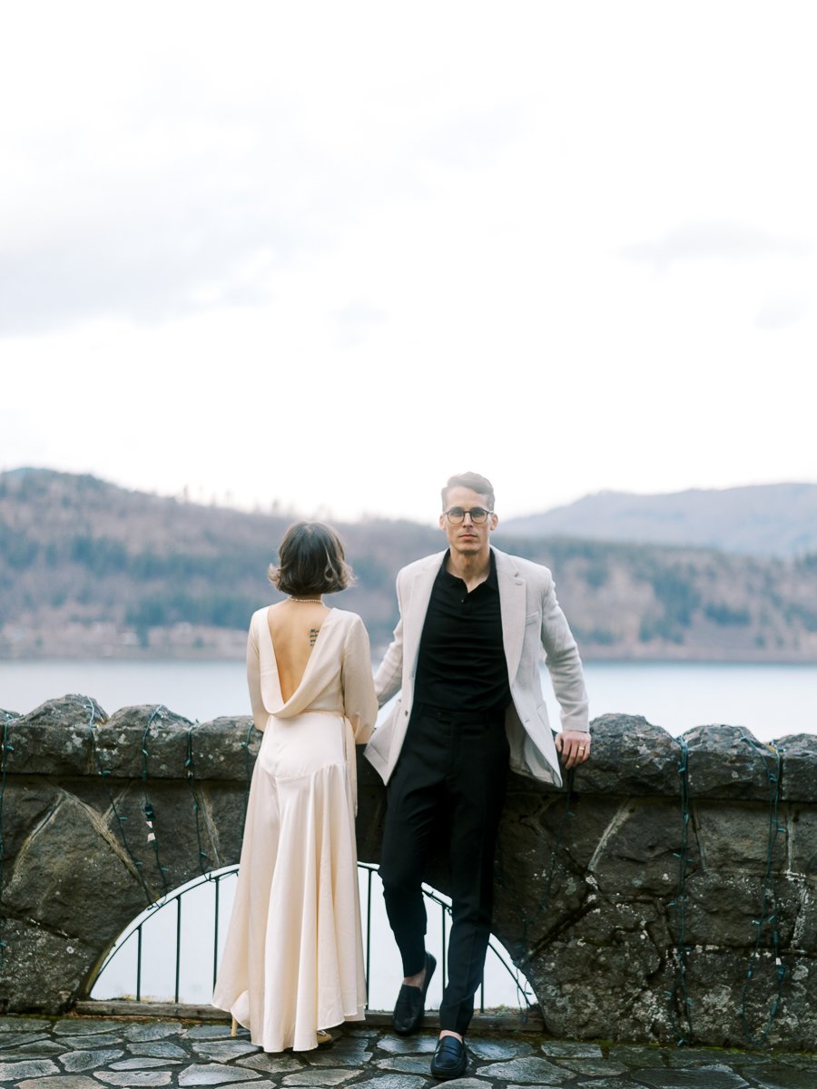 Bride in a silk gown and groom in a light blazer standing at a stone wall overlooking the Columbia River Gorge, captured on film.