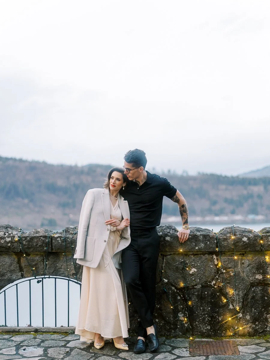 Couple leaning together against a stone wall strung with lights at the Columbia Gorge Hotel, photographed on color film at dusk.