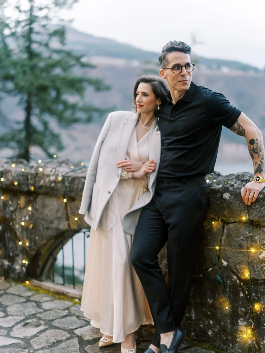 Editorial-style portrait of a couple resting against a stone wall overlooking the Columbia River Gorge, captured on film.