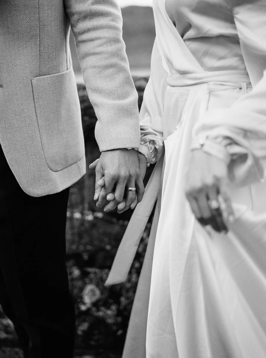 Close-up of the couple holding hands, wedding ring visible, photographed on black and white film.