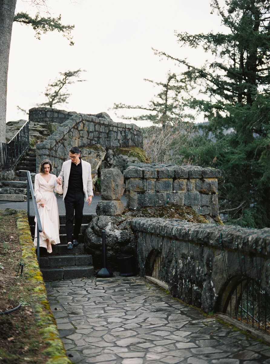 Couple descending stone steps at the Columbia Gorge Hotel, framed by historic masonry and evergreens, photographed on film.