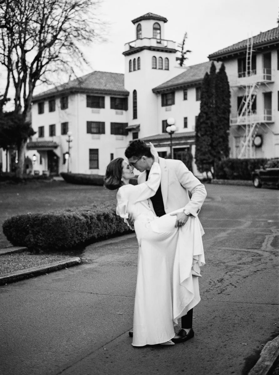 Black and white film portrait of the couple embracing in front of the Columbia Gorge Hotel, the tower rising behind them.