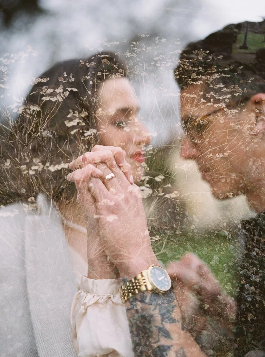 Double-exposure style film photograph of the couple holding hands, layered with wild grasses and soft motion.