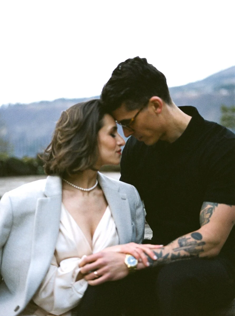 Color film portrait of the couple seated close together, foreheads touching, with the Columbia River Gorge softly blurred behind them.