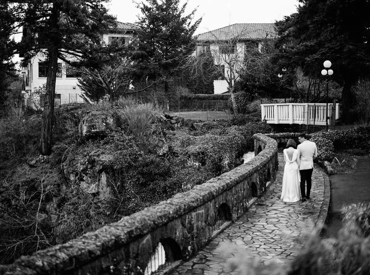 Couple walking away together across a curved stone bridge at the Columbia Gorge Hotel, captured in black and white film.