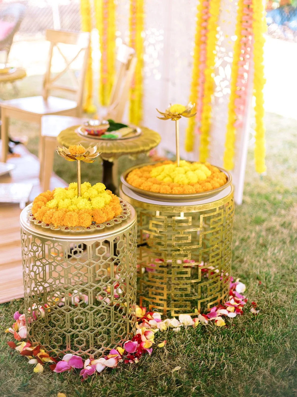 Gold decorative stands topped with yellow and orange marigolds, surrounded by petals on grass.