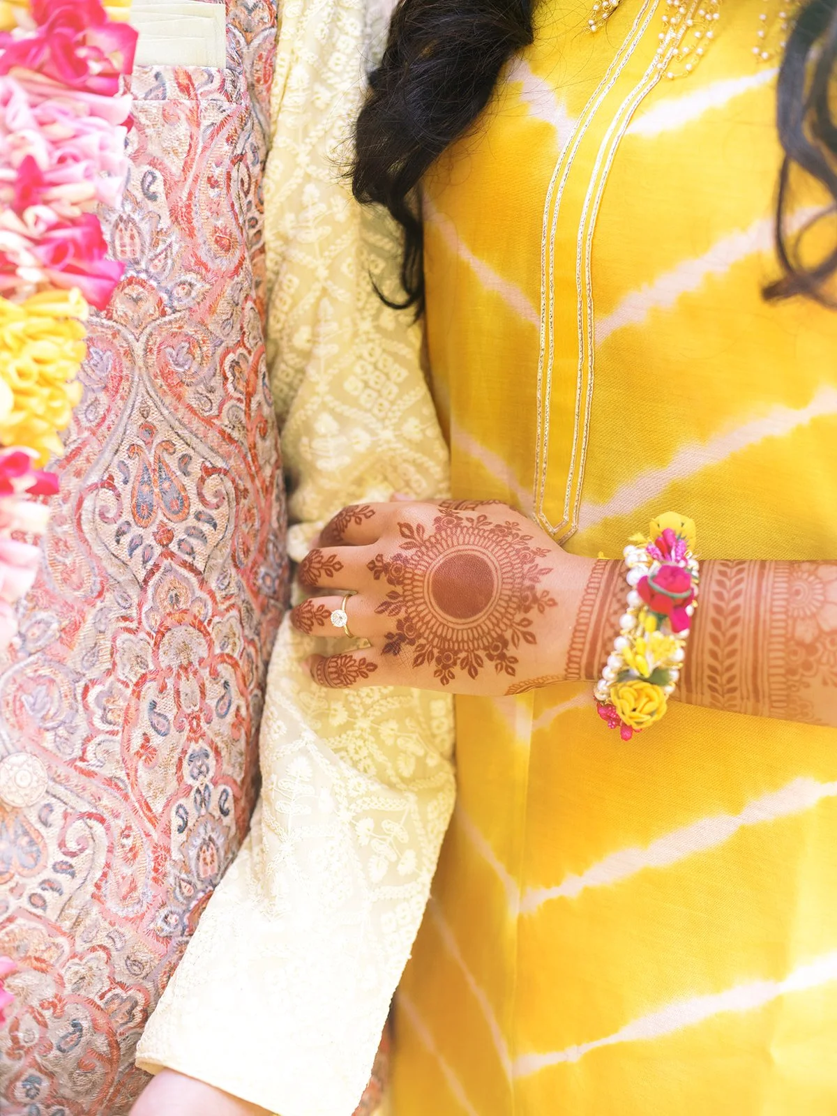 Close-up of intricate mehndi design on bride’s hand with floral bracelet against yellow traditional attire.