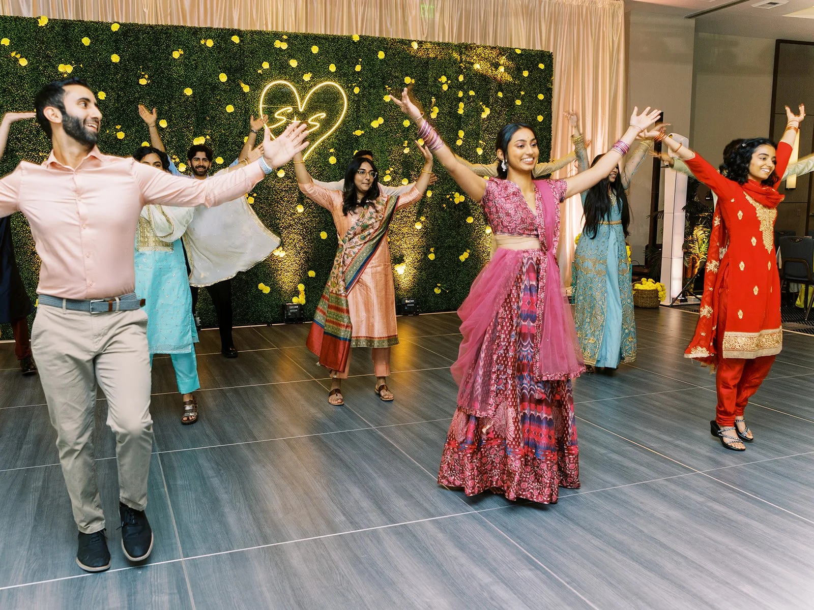 Guests in colorful traditional Indian outfits performing a coordinated dance at engagement celebration.