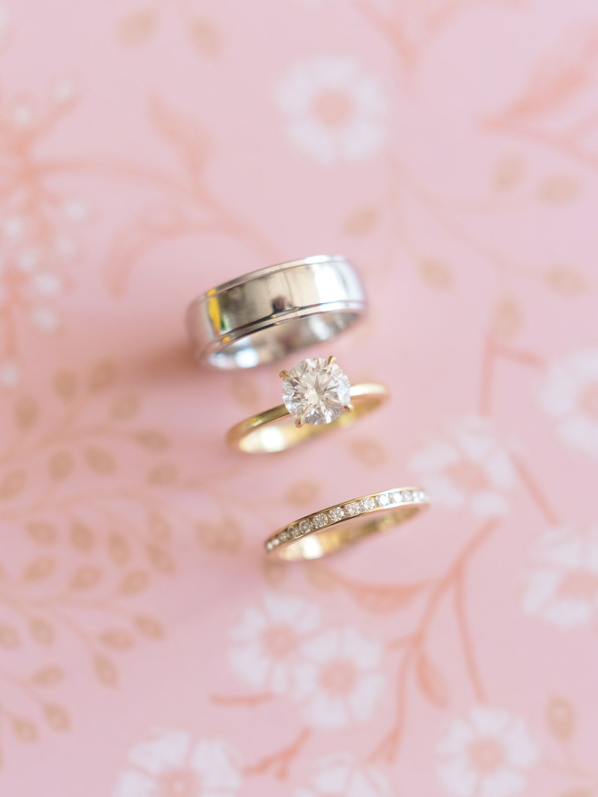 Diamond engagement ring and wedding bands arranged on soft pink floral wedding invitation.