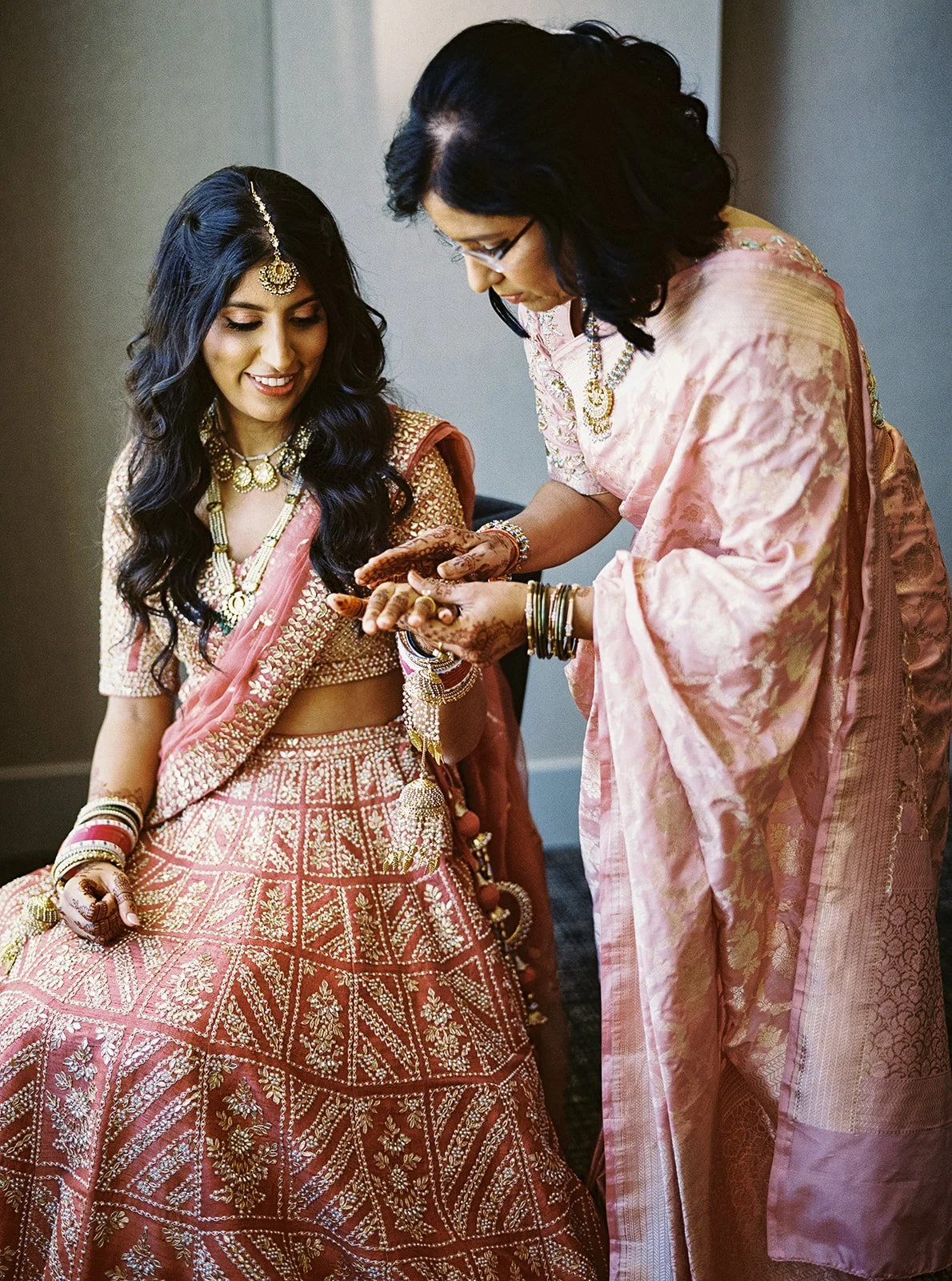 Mother in pink sari holding bride’s henna-adorned hands during getting ready moments.