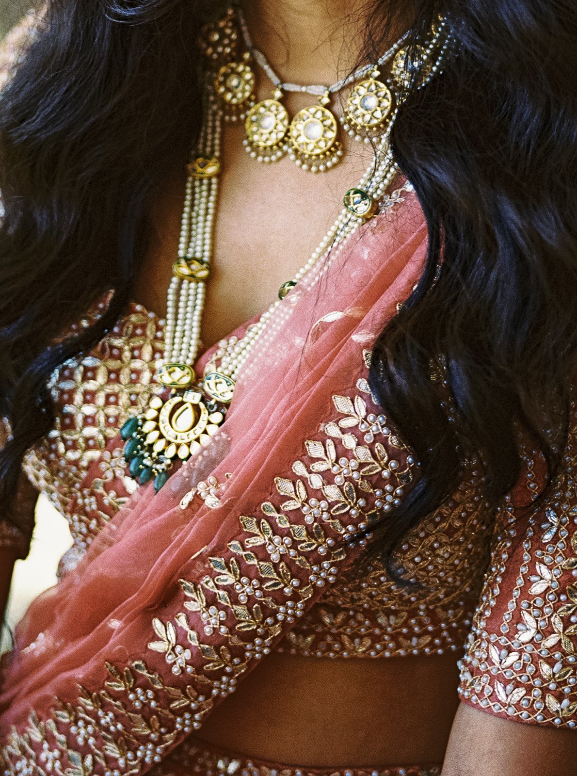 Close-up of bride’s gold necklace layered over embroidered red and gold lehenga.