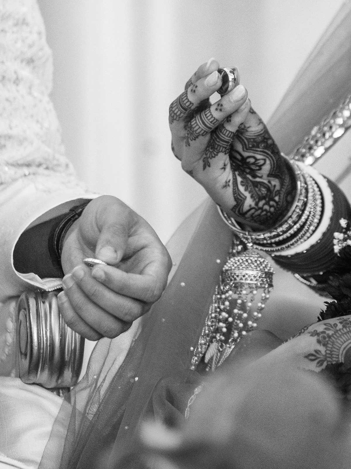 Black and white close-up of couple exchanging rings during Hindu wedding ceremony.