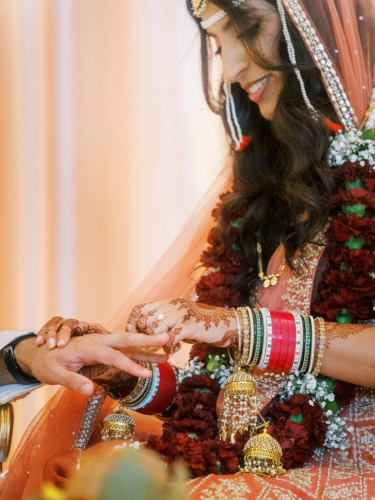 Bride placing wedding ring on groom’s finger, detailed mehndi and bangles visible.