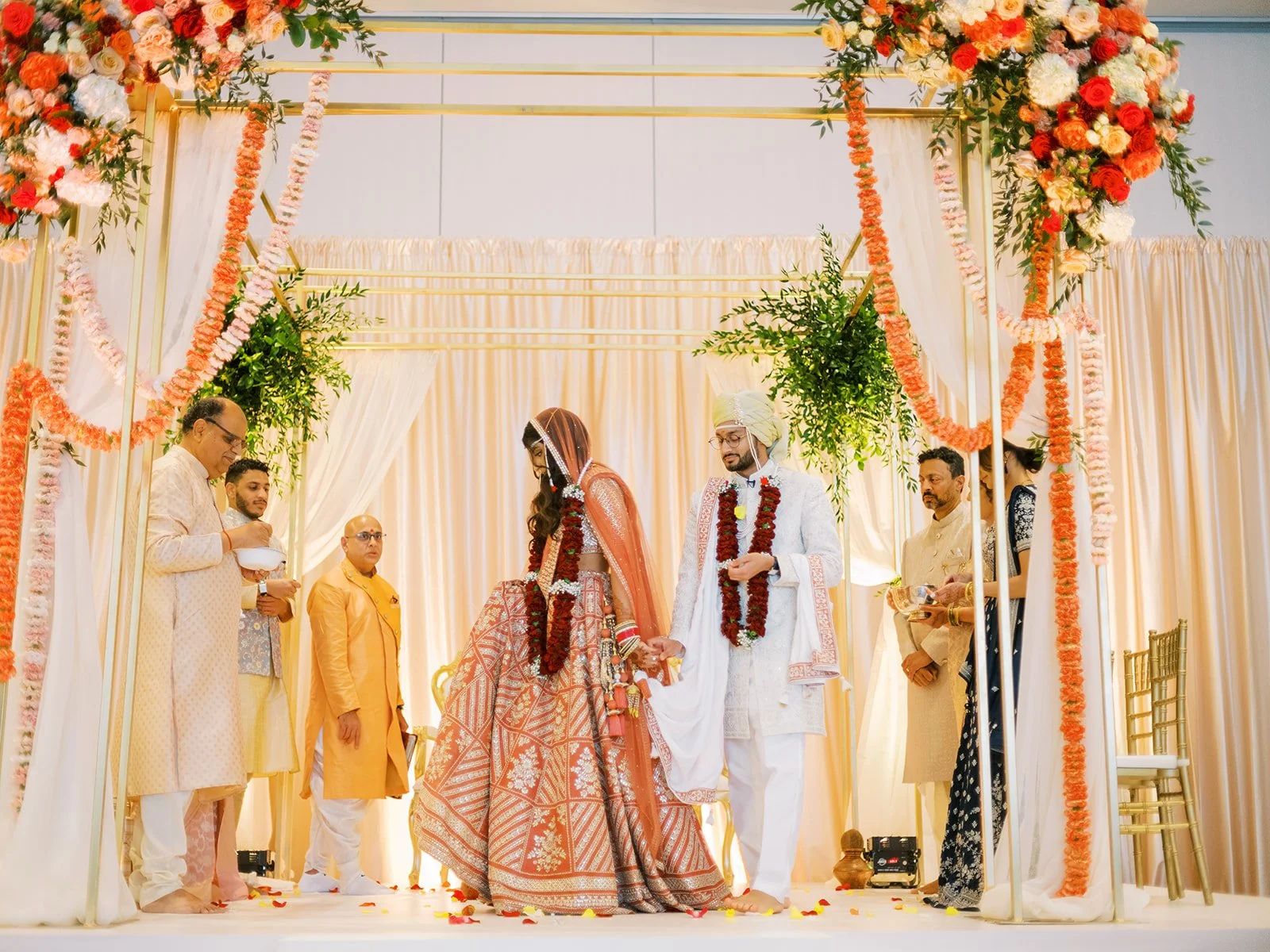 Bride and groom walking together under floral mandap during traditional Hindu wedding vows.