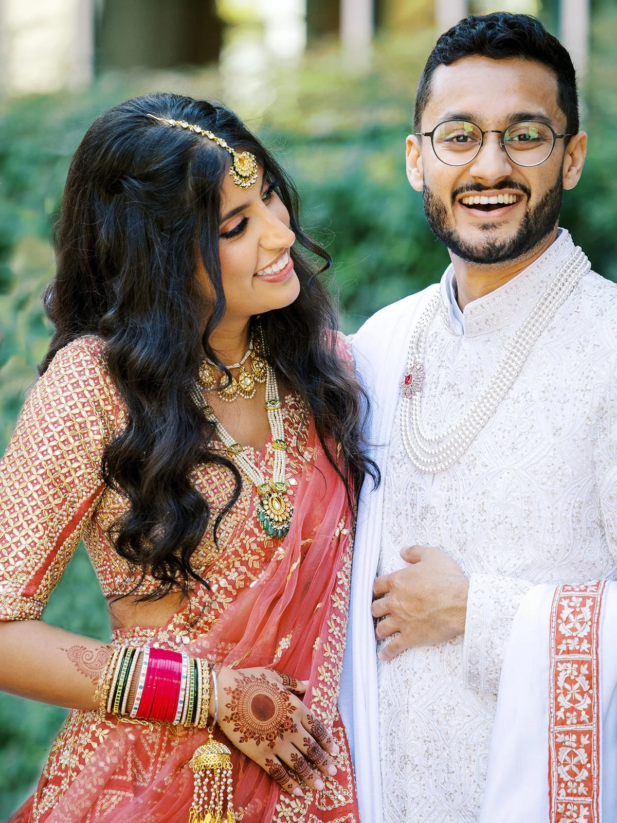 Close-up of bride in red lehenga smiling at groom in embroidered ivory sherwani.