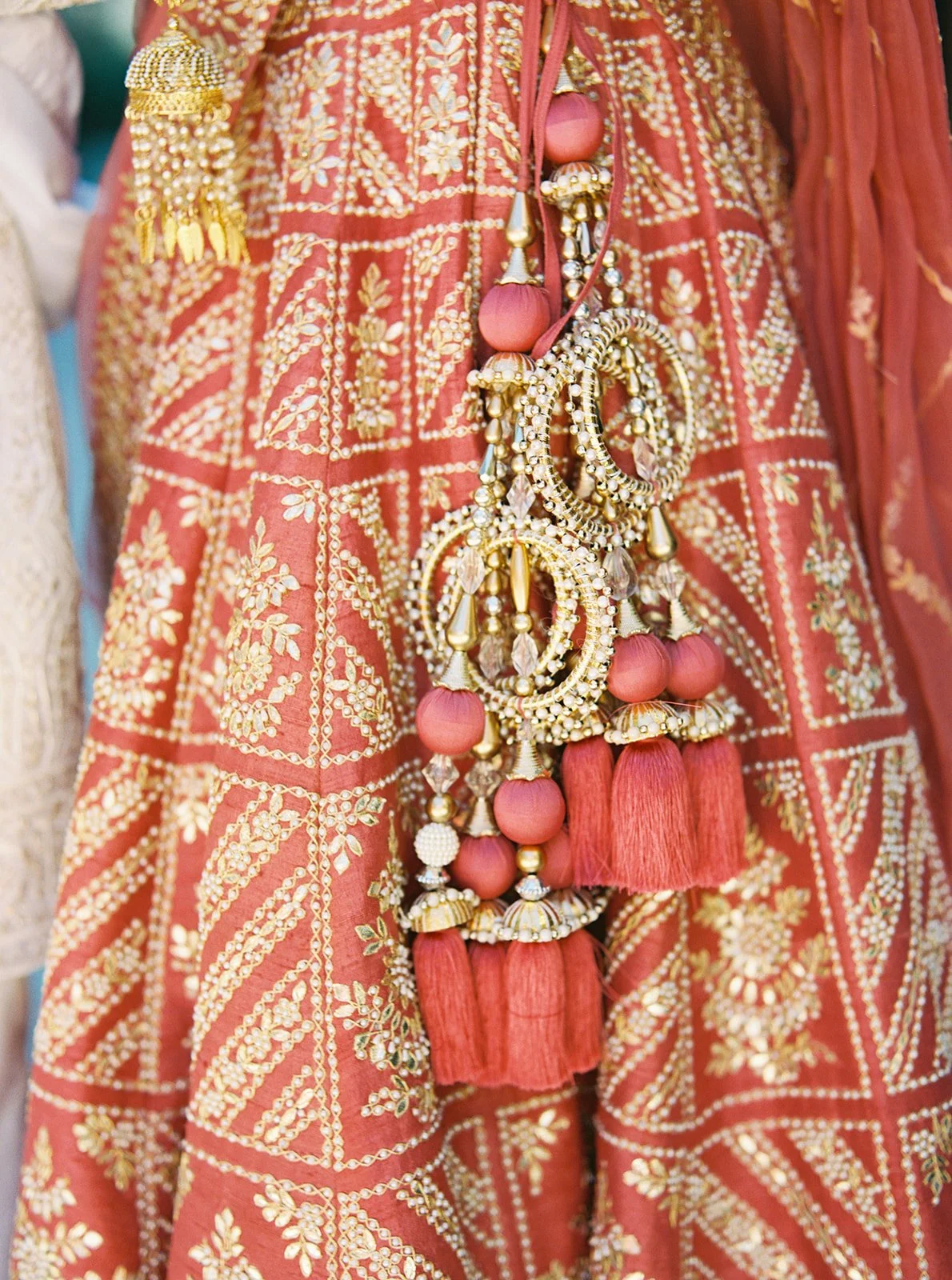 Detailed view of red and gold embroidered bridal lehenga with dangling tassels and ornaments.