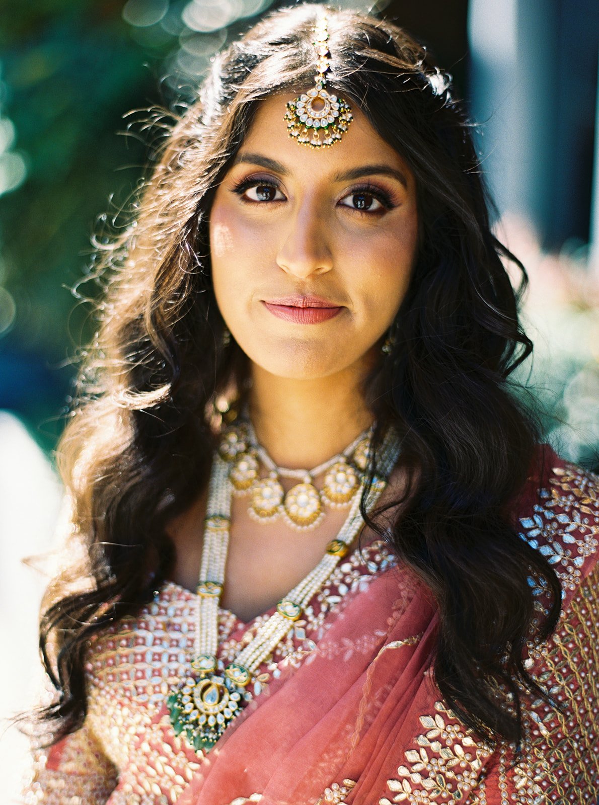 Close-up bridal portrait highlighting gold maang tikka, layered necklace, and red bridal outfit.