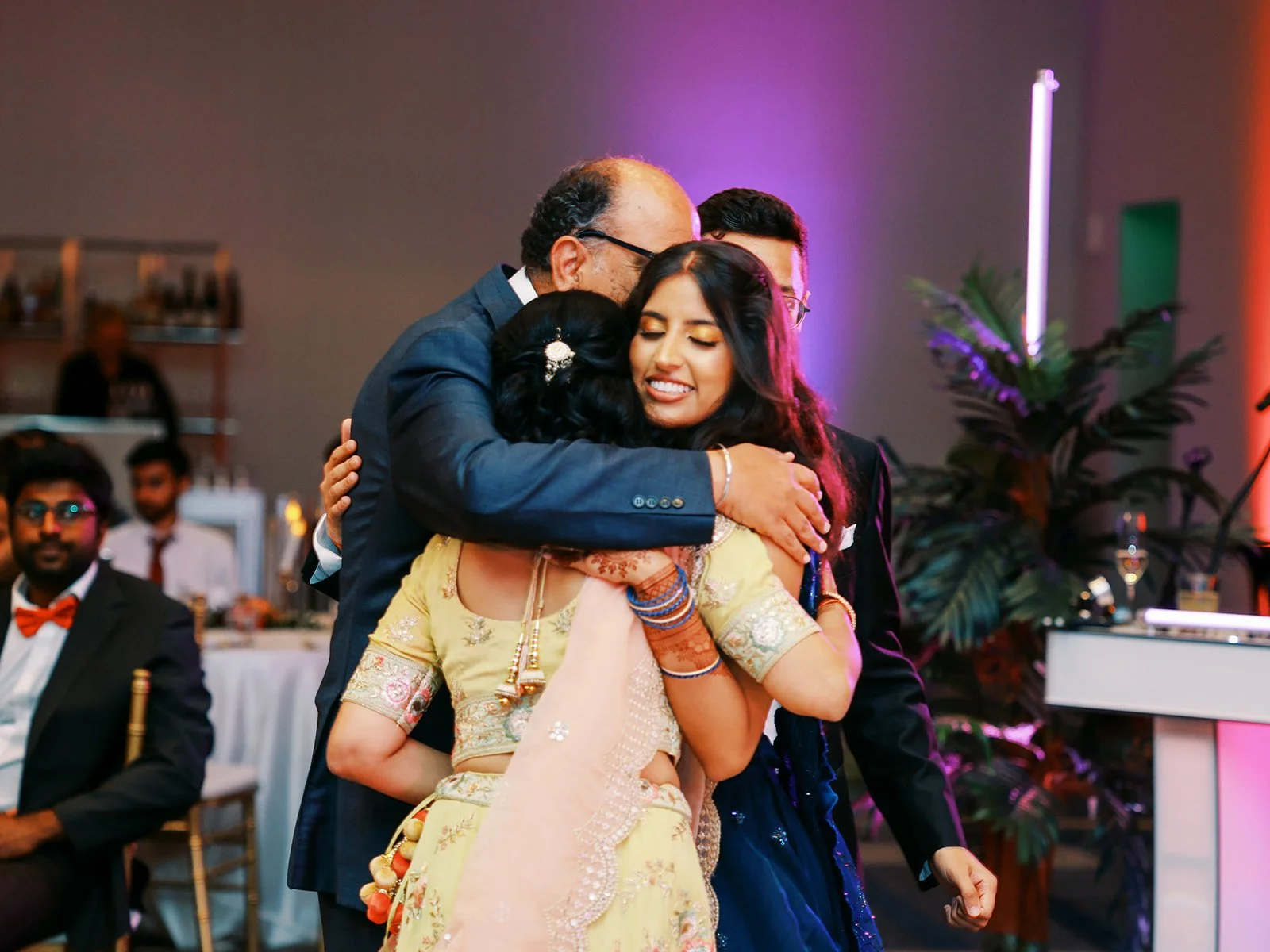 Bride in navy lehenga embracing family members during emotional reception moment.