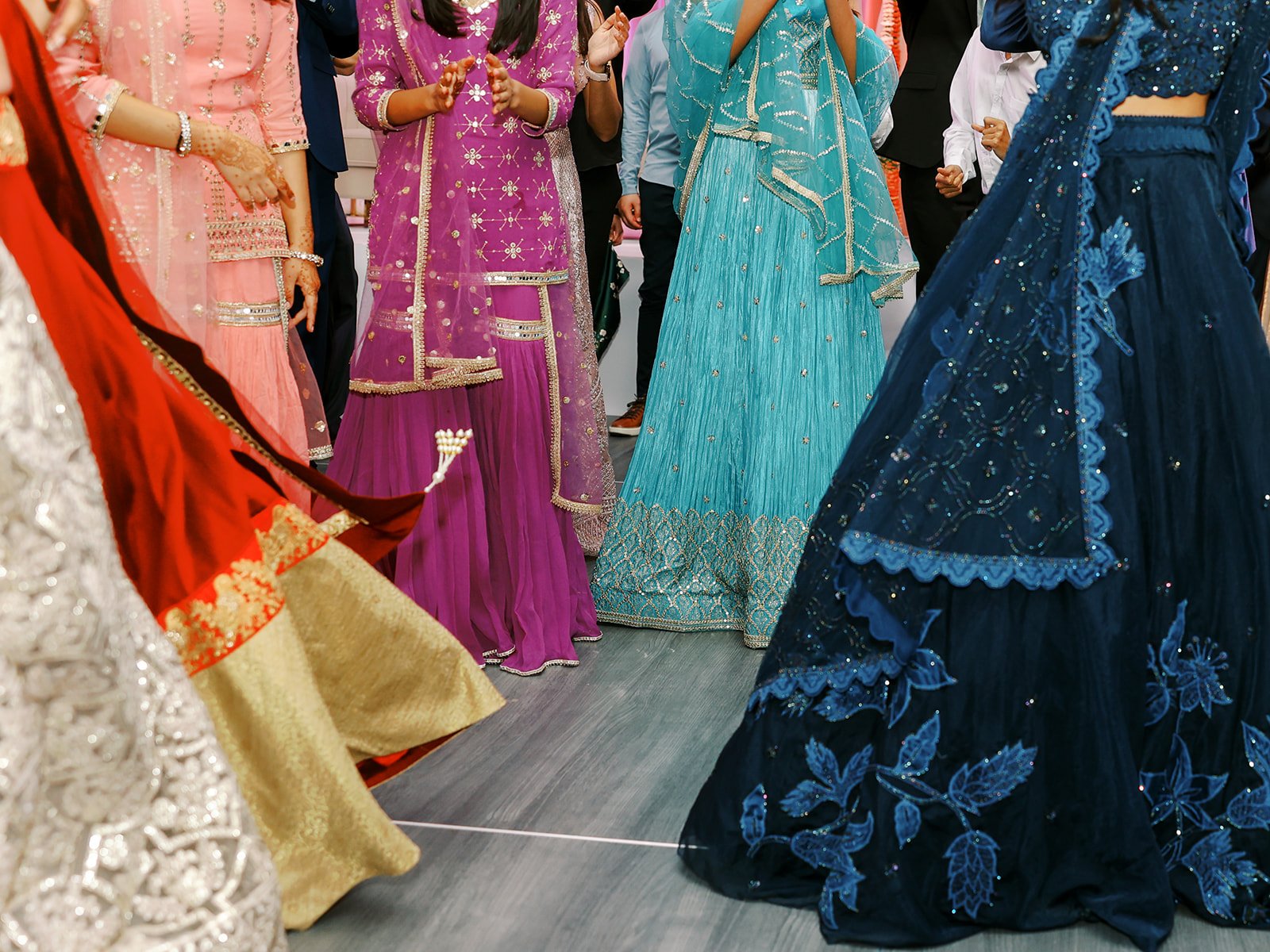 Close-up of colorful embroidered lehengas and salwar suits swirling on the dance floor.