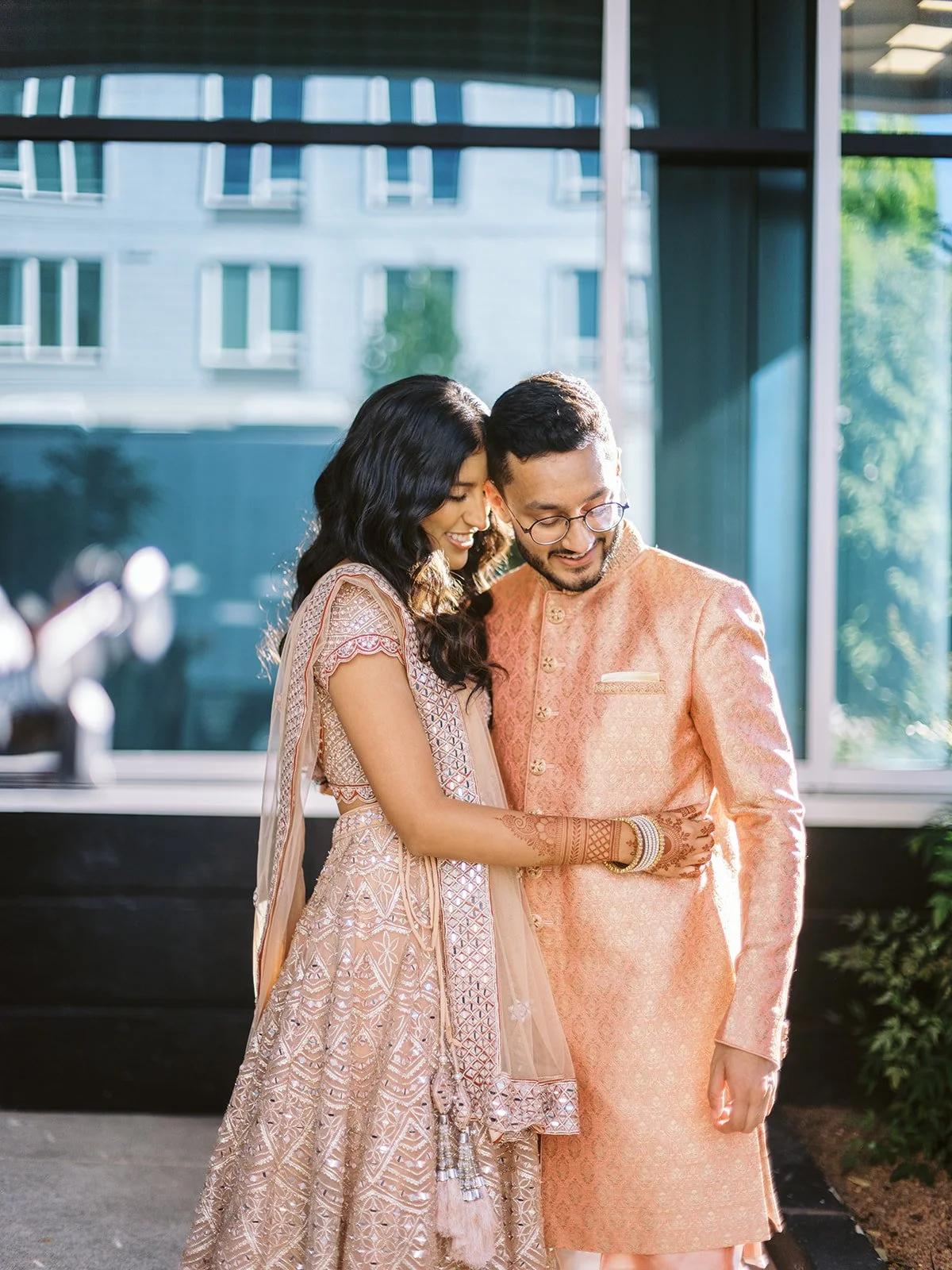 Couple in coordinated peach traditional outfits standing close outside a modern venue.