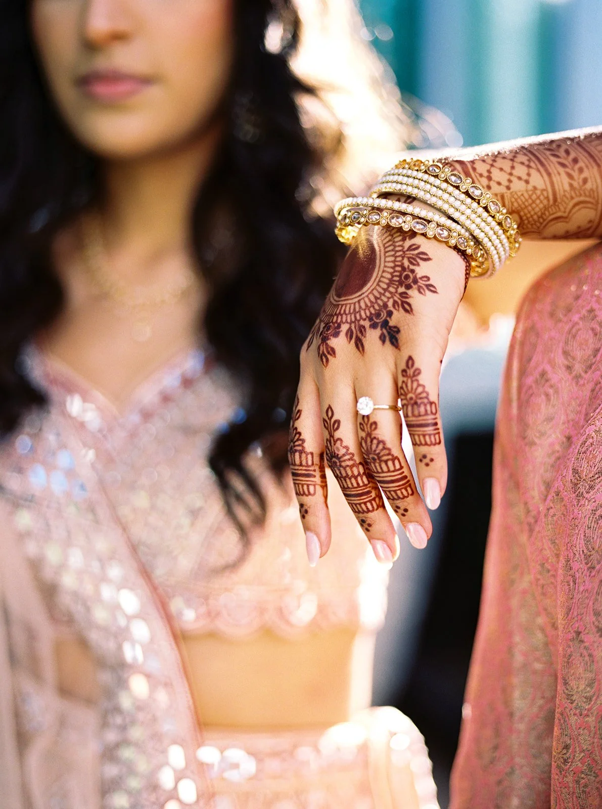 Close-up of bride’s hand with detailed mehndi, gold bangles, and solitaire engagement ring.
