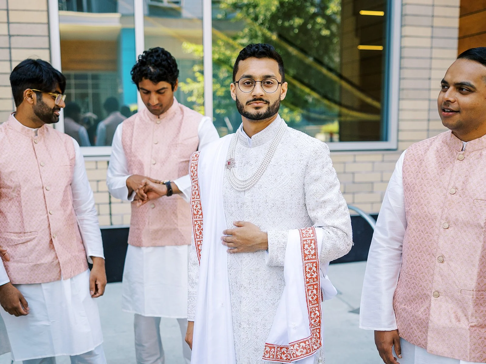 Groom in ivory sherwani standing confidently with groomsmen in blush waistcoats.