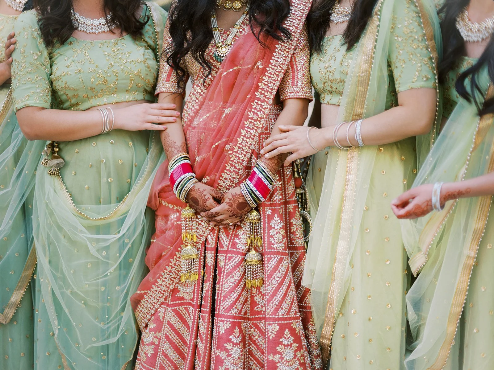 Close-up of bride in red lehenga surrounded by bridesmaids in matching green outfits.