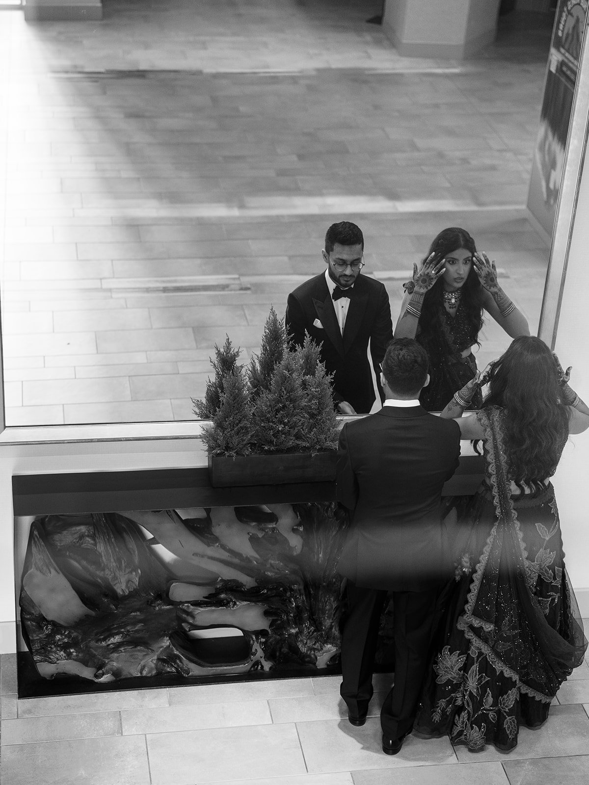 Aerial black and white shot of a couple in wedding attire beside a decorative planter inside a hotel lobby.